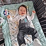 baby, crib, overalls, bib, toy, blanket, smiling, happy, indoor, child, footwear, white_shoes, patterned_blanket, soft_toys, wooden_floor, playpen, infant, cute, lying_down, clothing