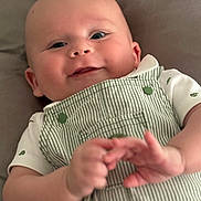Simon is registered to the contest to win money with this photo: baby, smile, face, hands, overalls, clothing, infant, lying_down, cute, child, portrait, skin, cheeks, white_shirt, button, green, striped, happy, person, soft_background