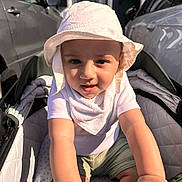 Yus is registered to the contest to win money with this photo: toddler, child, baby, stroller, hat, sun_hat, bib, shorts, outdoor, daylight, car, vehicle, urban, person, infant, cute, curious, hands, face, expression