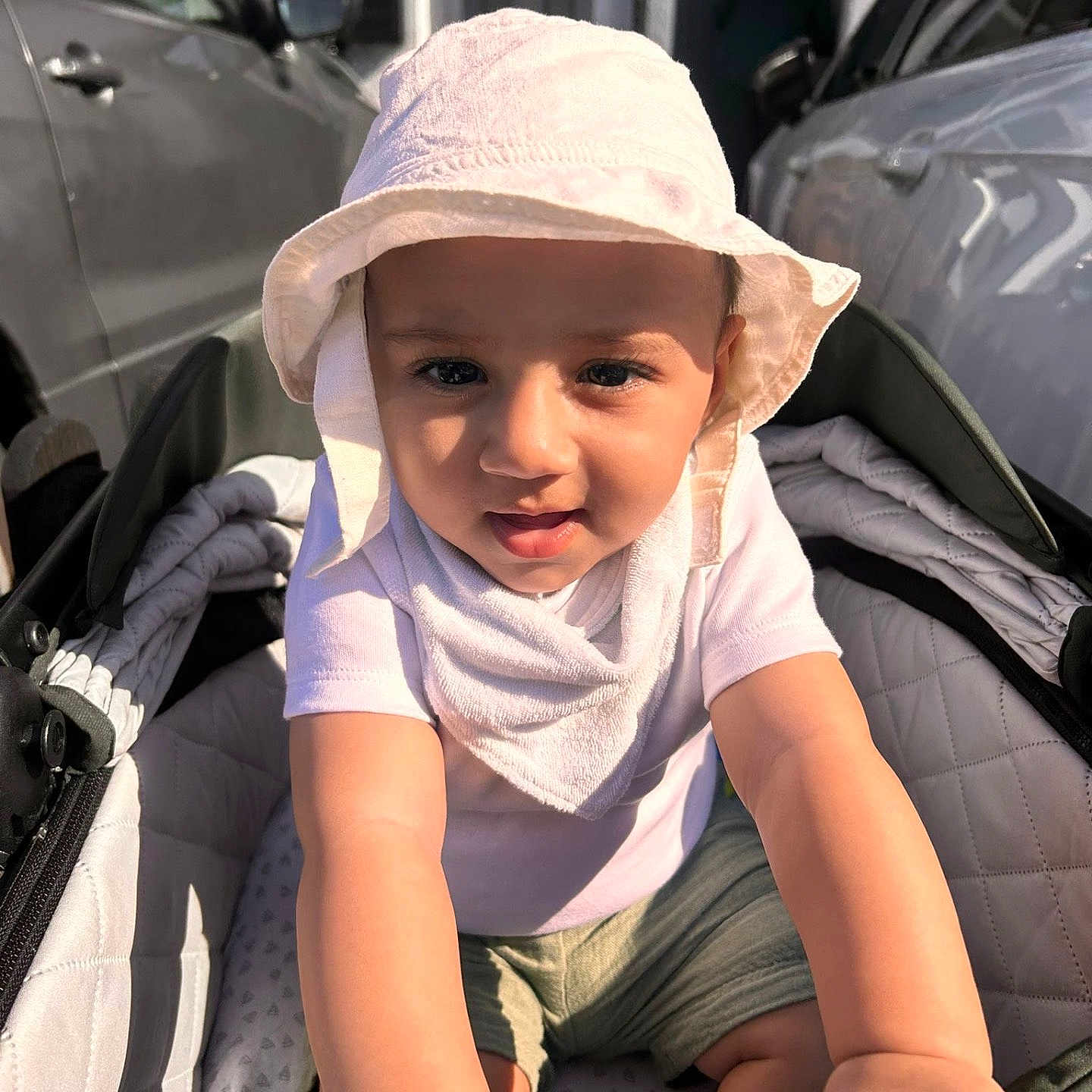 Yus is registered to the contest to win money with this photo: baby, bib, car, child, curious, cute, daylight, expression, face, hands, hat, infant, outdoor, person, shorts, stroller, sun_hat, toddler, urban, vehicle