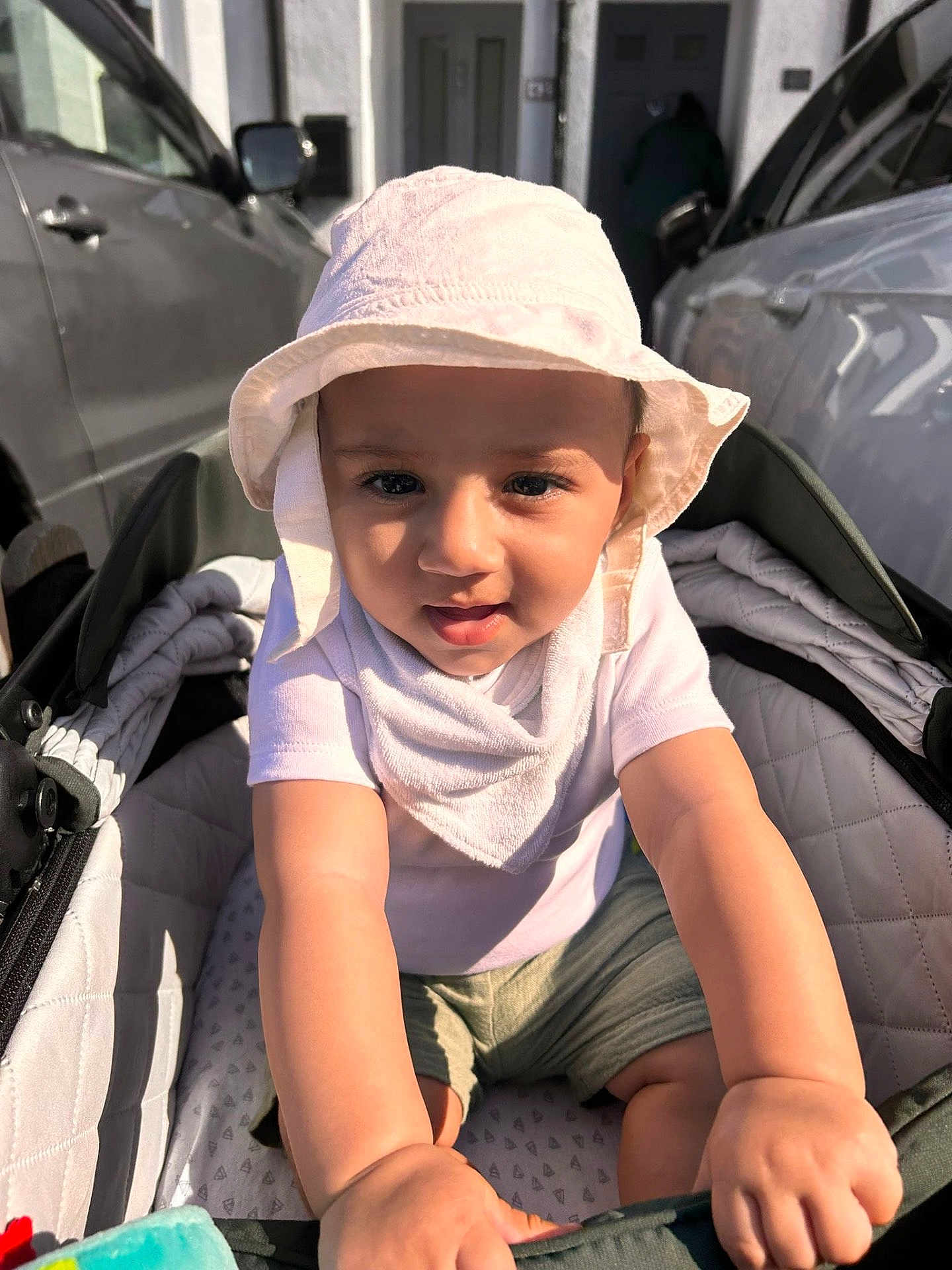 Yus is registered to the contest to win money with this photo: toddler, child, baby, stroller, hat, sun_hat, bib, shorts, outdoor, daylight, car, vehicle, urban, person, infant, cute, curious, hands, face, expression