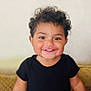 toddler, child, smiling, curly_hair, black_shirt, happy, standing, indoors, face, portrait, cute, young_child, person, skin, human, hair, eyes, mouth, expression, background