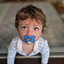 toddler, child, pacifier, blue_pacifier, curious, wide_eyes, hands, wooden_floor, indoor, soft_focus, blurry_background, striped_clothing, baby, cute, portrait, crawling, young_child, innocent, hair, looking_up