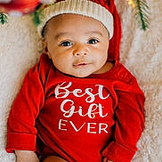 Arlo joined the competition — help win amazing prizes! baby, infant, red_onesie, holiday_hat, christmas, festive, blanket, face, smile, cute, child, portrait, indoors, soft_lighting, holiday_decor, greenery, warm_lights, cozy, happy, person