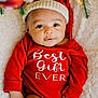 baby, infant, red_onesie, holiday_hat, christmas, festive, blanket, face, smile, cute, child, portrait, indoors, soft_lighting, holiday_decor, greenery, warm_lights, cozy, happy, person