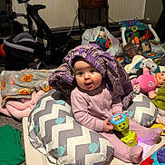 Saivanii is registered to the contest to win money with this photo: baby, blanket, car_seat, cheek, chevron_pattern, clutter, floor_play, indoor, infant, nursery_items, onesie, pillow, playmat, plush_toy, purple_bonnet, rattle, sitting, smile, toy, wide_eyes