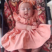 Bentley is registered to the contest to win money with this photo: baby, child, cute, dress, headband, winking, smiling, blanket, patterned, seated, infant, hands, feet, indoors, colorful, clothing, fabric, portrait, happy, playful