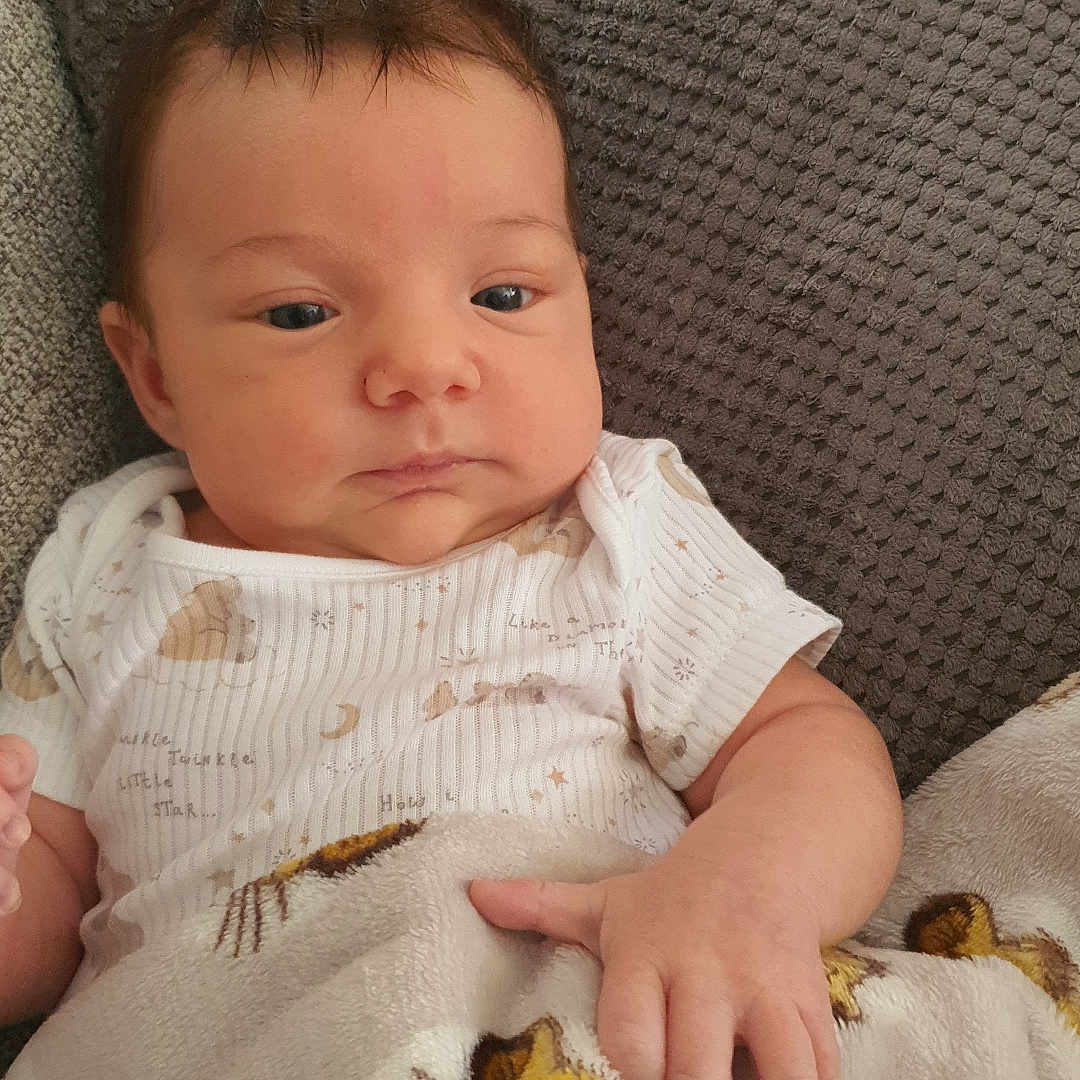 Dante is registered to the contest to win money with this photo: baby, blanket, cartoon, child, clothing, cozy, cushion, cute, gray, indoor, infant, lion, person, portrait, resting, small_hand, soft, texture, white, young