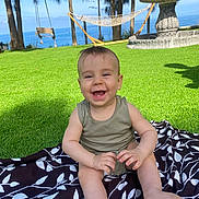 Ilyan participe au concours pour gagner de l'argent avec cette photo : baby, child, grass, outdoor, smiling, happy, blanket, nature, trees, blue_sky, sunlight, infant, playful, summer, portrait, grass_field, sitting, clothing, fence, fountain