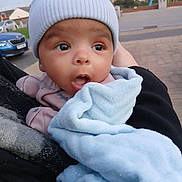Kaeden is registered to the contest to win money with this photo: baby, infant, hat, blanket, outdoor, street, car, person, clothing, headwear, expression, holding, curious, cozy, child, face, warm, ears, urban, daylight