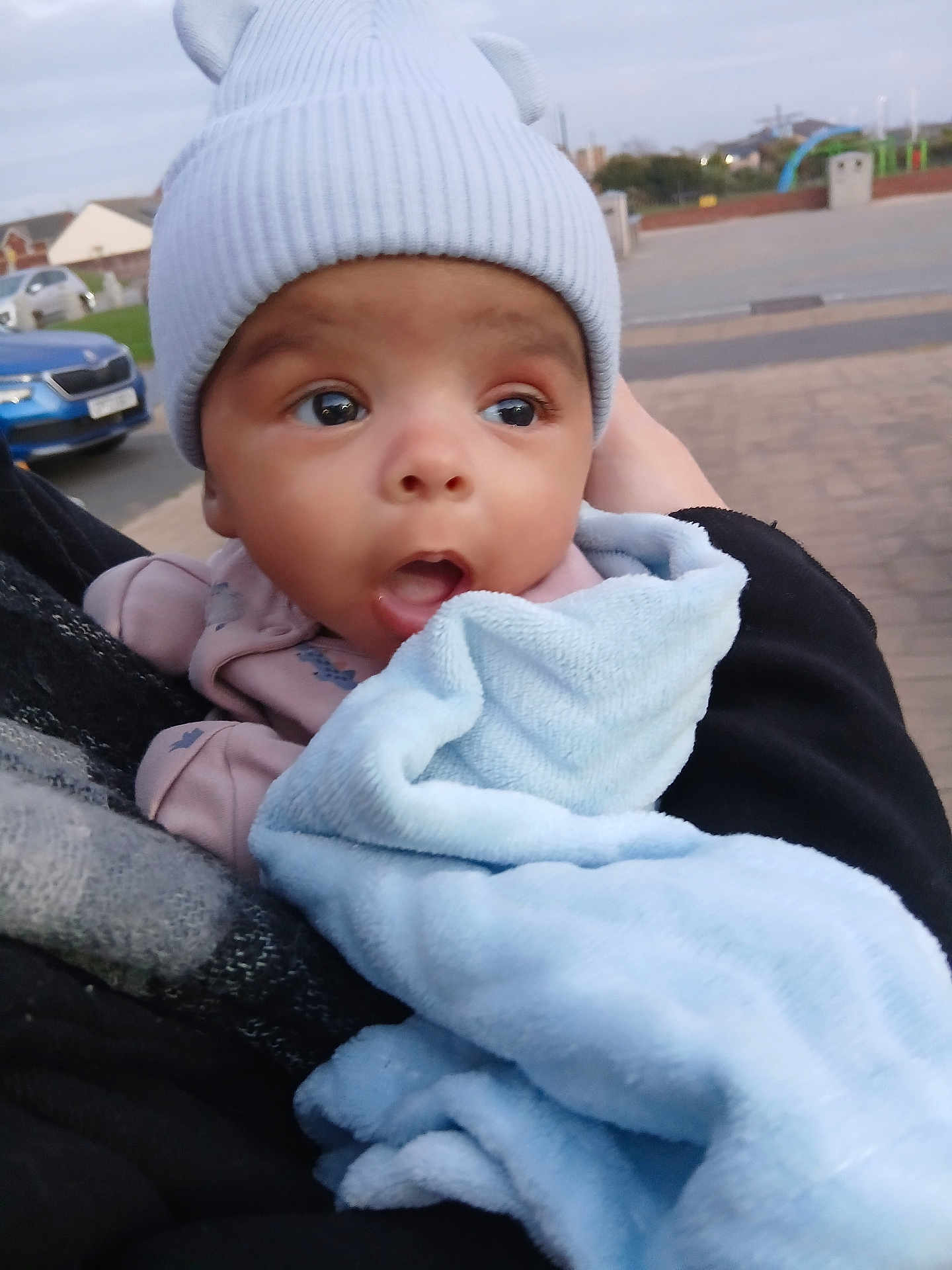 Kaeden is registered to the contest to win money with this photo: baby, infant, hat, blanket, outdoor, street, car, person, clothing, headwear, expression, holding, curious, cozy, child, face, warm, ears, urban, daylight