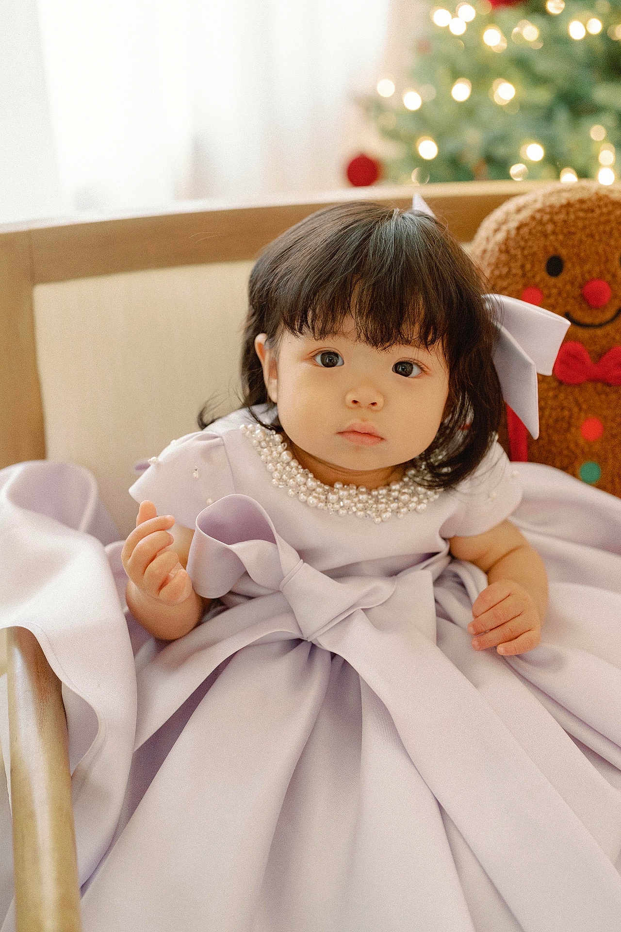 Muriel Kim is registered to the contest to win money with this photo: toddler, child, dress, lavender, pearl_necklace, chair, wooden, gingerbread_man, plush_toy, christmas_tree, holiday, indoors, curly_hair, portrait, cute, baby, smile, festive, soft_light, decor
