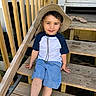 Leonardo is registered to the contest to win money with this photo: child, boy, hat, smiling, sitting, wooden_steps, outdoor, casual_clothing, blue_shorts, white_socks, railing, sandals, daylight, happy, young, portrait, wood, stairs, relaxed, person