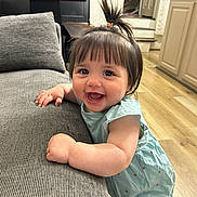 Lydia joined the competition — help win amazing prizes! baby, child, smile, happy, indoor, living_room, couch, furniture, hair, pony_tail, floor, wood_floor, dress, blue_dress, hand, face, cute, person, infant, home