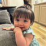 Lydia joined the competition — help win amazing prizes! baby, blue_dress, cheerful, child, couch, curly_hair, cute, face, furniture, hand_in_mouth, happy, home, indoor, infant, person, pony_tail, portrait, smiling, wood_floor, young_child