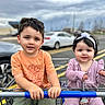 baby, boy, car, casual_clothing, child, children, cute, daytime, face, girl, hands, headband, orange_shirt, outdoor, parking_lot, person, purple_outfit, shopping_cart, smiling, toddler