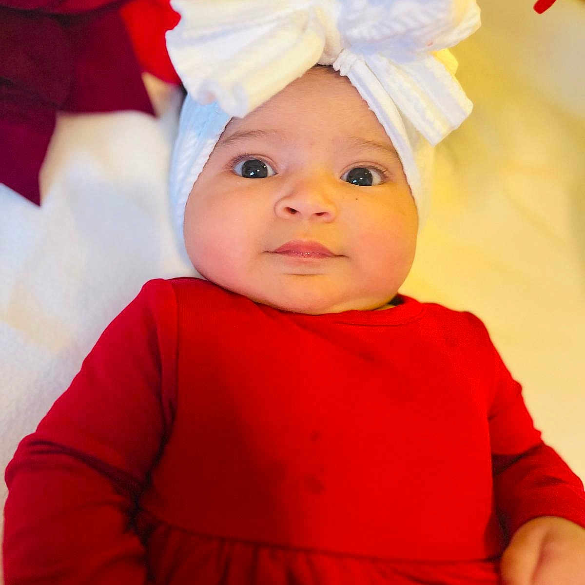 Katalyna is registered to the contest to win money with this photo: baby, blanket, child, closeup, cozy, cute, expression, eyes, face, hand, headwear, holiday, indoor, infant, newborn, person, portrait, red_clothing, soft_fabric, white_bow