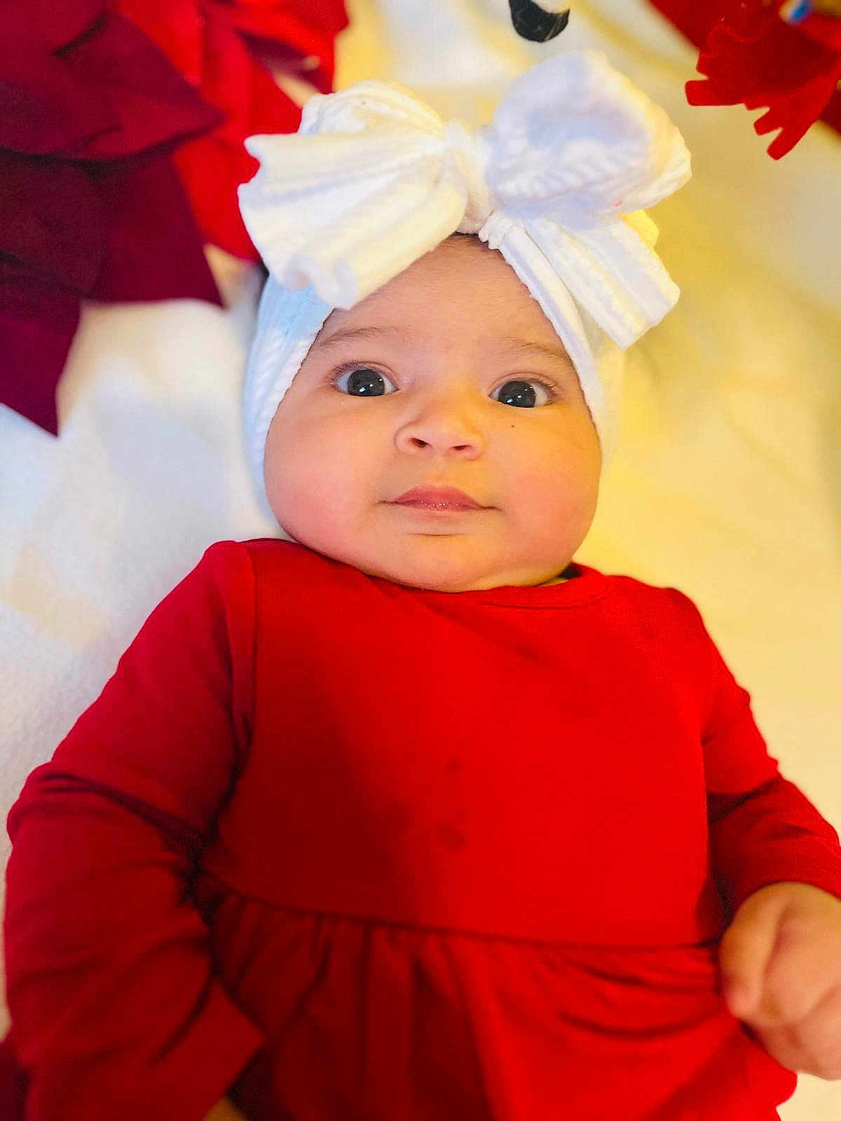 Katalyna is registered to the contest to win money with this photo: baby, infant, child, red_clothing, white_bow, headwear, face, eyes, hand, portrait, indoor, soft_fabric, blanket, cute, expression, person, closeup, newborn, holiday, cozy