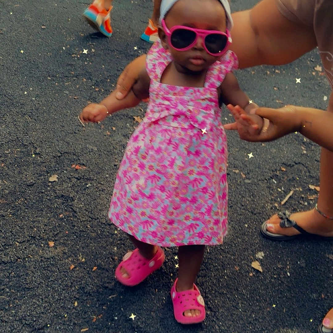 Emani joined the competition — help win amazing prizes! toddler, child, pink_dress, sunglasses, headband, outdoor, walking, adult_hand, support, pavement, casual_clothing, sandals, person, summer, star_effects, nature, grass, tree, sidewalk, fun