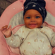 Emani is registered to the contest to win money with this photo: baby, infant, smiling, head_wrap, onesie, pink_cushion, seat, happy, portrait, indoors, child, cute, cozy, face, small_hand, expression, comfort, sparkles, fabric, closeup