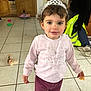 toddler, child, tiara, pink_sweater, purple_pants, red_socks, indoor, tile_floor, toy_doll, snack, curly_hair, smiling, person, home, casual_clothing, playful, floor_tiles, background, household_items, cozy