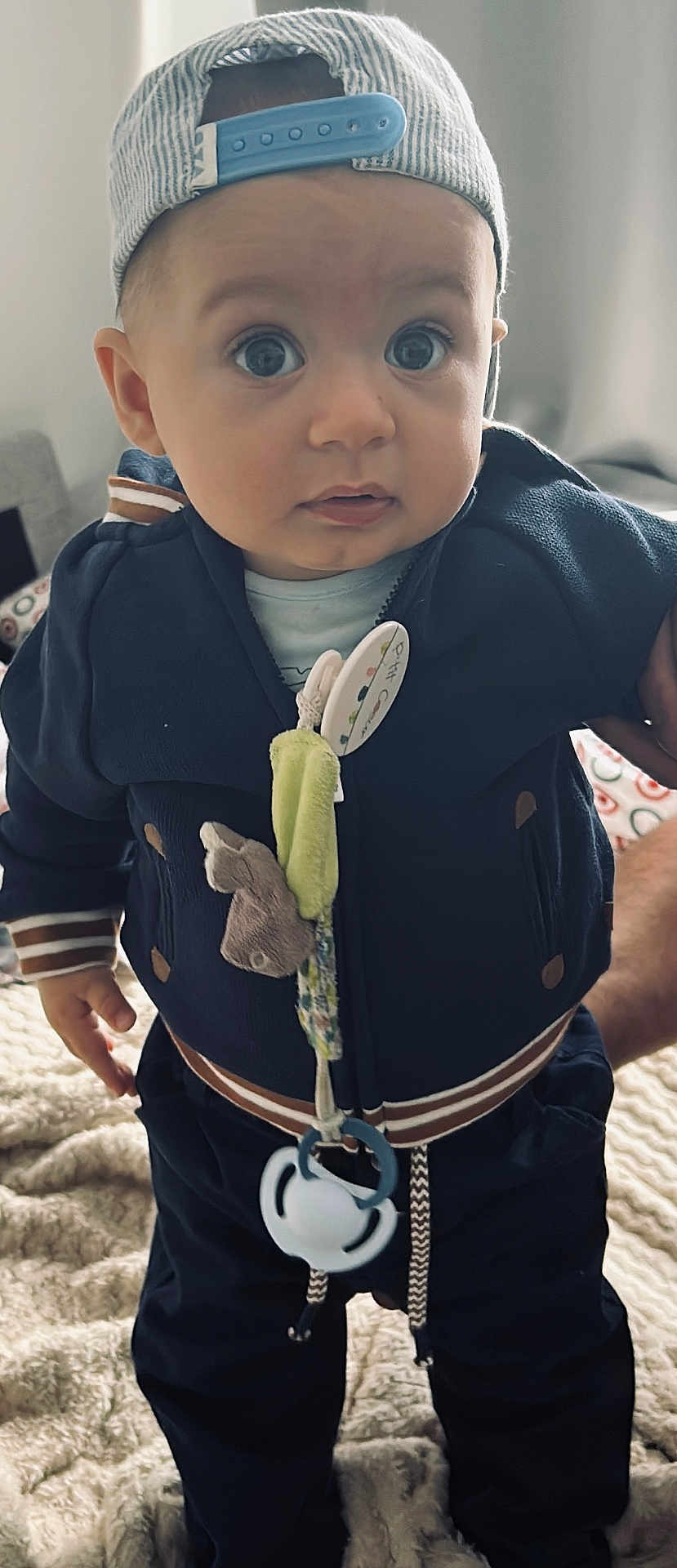 Djamal a rejoint le concours — aidez-le/la à gagner de superbes lots ! baby, child, indoor, clothing, jacket, cap, face, pacifier, toy, blanket, hand, person, curious, wide_eyes, standing, cute, infant, apparel, striped, soft
