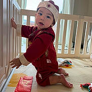 Ehaan is registered to the contest to win money with this photo: baby, toddler, crib, playpen, red_envelope, hat, traditional_clothing, mat, toy, barefoot, kneeling, smile, portrait, indoor, window, curtain, floor, hand, cute, playtime
