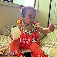 Tania is registered to the contest to win money with this photo: baby, toddler, child, orange_clothing, bows, bed, window, natural_light, indoor, playing, accessories, foot, hand, curious, portrait, person, room, blanket, fabric, candid
