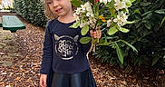 Alina is registered to the contest to win money with this photo: bench, bouquet, casual_clothing, child, daylight, fallen_leaves, flowers, garden, girl, greenery, leaves, long_sleeves, nature, outdoor, person, pink, shoes, skirt, smile, white_flowers