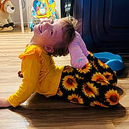 Alina is registered to the contest to win money with this photo: child, smiling, yellow_clothing, sunflower_pants, pink_socks, wooden_floor, rocking_lion_toy, baby_chair, indoor, playful_pose, happy, person, flooring, toys, colorful, cute, young_child, home, fun, playtime