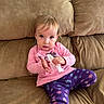 toddler, child, pink_shirt, purple_leggings, snowflake_pattern, brown_couch, indoor, casual, clothing, sitting, curious, face, person, young_child, tissue, home, cozy, portrait, expression, furniture