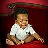 baby, child, smiling, sitting, white_shirt, polo_shirt, red_sofa, velvet_sofa, indoor, cute, happy, portrait, infant, person, furniture, curly_hair, young_child, bright_eyes, barefoot, cozy