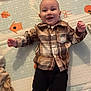 baby, smiling, plaid_shirt, pants, play_mat, infant, lying_down, happy, child, footwear, indoor, cute, face, person, young, clothing, pattern, baby_toys, colorful, background