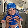 baby, blue_clothing, blue_hat, casual, child, couch, cute, diaper, face, hands, happy, holding, indoor, infant, kitchen, modern_home, person, portrait, sitting, smile