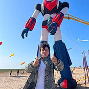 Mauricio participe au concours pour gagner de l'argent avec cette photo : boy, child, thumbs_up, camouflage_jacket, robot_kite, beach, sand, blue_sky, kite_flying, people, outdoor, daytime, smiling, casual_clothing, fun, recreation, vacation, sunny, leisure, event
