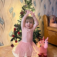 Pereira Marcia a rejoint le concours — aidez-le/la à gagner de superbes lots ! toddler, child, pink_tutu, christmas_tree, holiday_lights, toy_unicorn, living_room, brown_couch, wallpaper, floor_tiles, smiling, happy, indoor, holiday_decor, person, plush_toy, festive, cute, barefoot, home