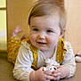 baby, child, closeup, curly_hair, cute, face, floor, hands, happy, indoor, infant, lying_down, person, play, portrait, smile, soft_lighting, toy, white_clothing, yellow_clothing