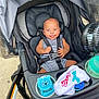 baby, stroller, infant, smiling, striped_clothing, baby_toys, pacifier, fan, seat_belt, outdoor, child, cute, happy, baby_bib, plastic_toy, fabric, black_seat, safety_harness, skin, head