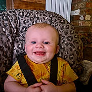 Finlay is registered to the contest to win money with this photo: baby, child, smiling, happy, infant, yellow_shirt, animal_print, high_chair, leopard_print, indoor, seat_belt, wooden_background, brick_wall, hands, face, cute, portrait, baby_clothing, human, young_child