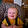 baby, child, smiling, happy, infant, yellow_shirt, animal_print, high_chair, leopard_print, indoor, seat_belt, wooden_background, brick_wall, hands, face, cute, portrait, baby_clothing, human, young_child