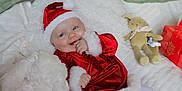 Abigael participe au concours pour gagner de l'argent avec cette photo : baby, santa_hat, red_clothing, white_blanket, plush_toy, gift_box, holiday, festive, smiling, cute, infant, cozy, soft_toy, christmas, lying_down, happy, white_tights, indoors, child, celebration