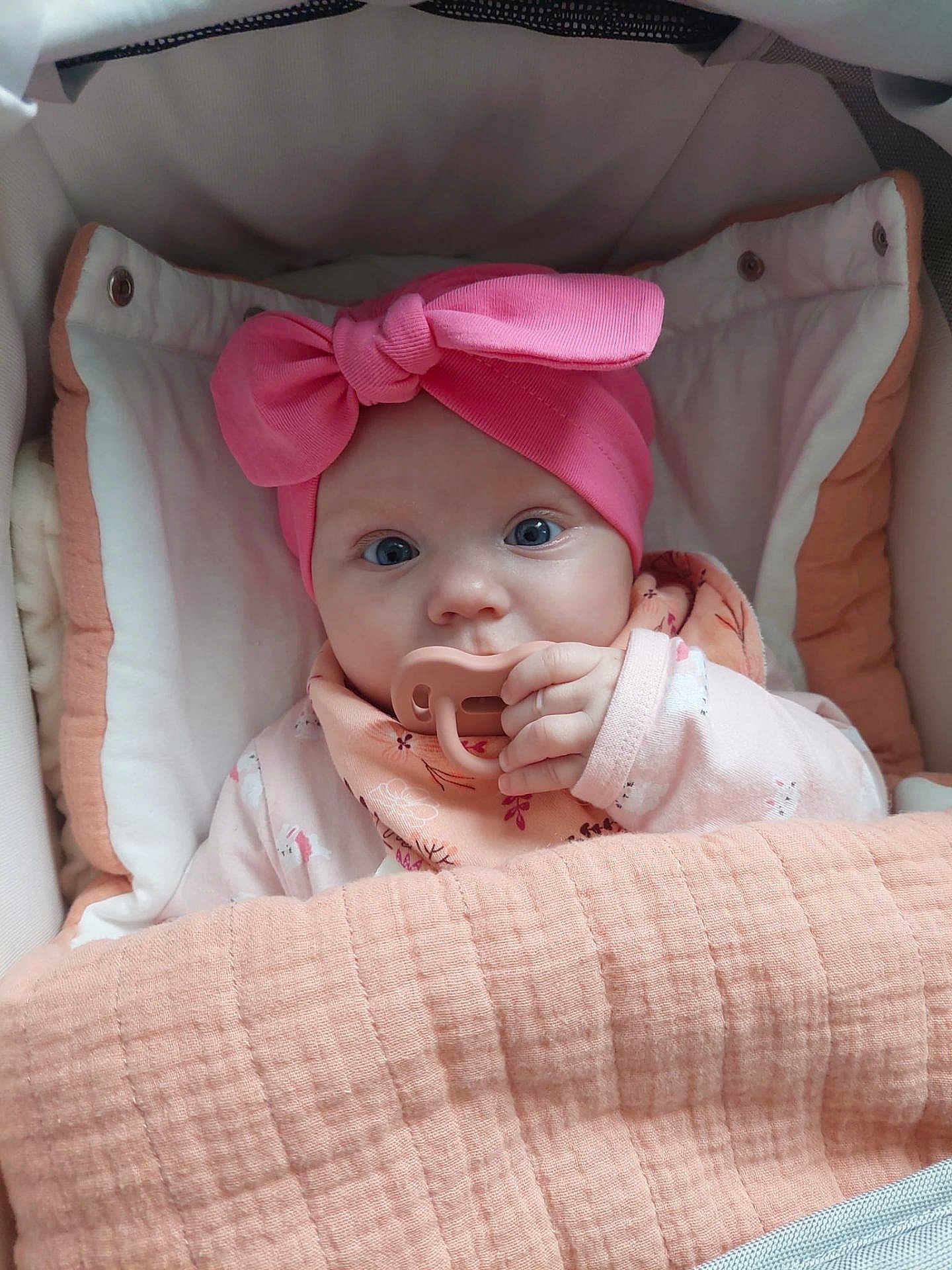 Abigael participe au concours pour gagner de l'argent avec cette photo : baby, child, pacifier, headband, pink_bow, blanket, cushion, stroller, blue_eyes, infant, cozy, cute, clothing, portrait, hand, face, indoors, sleepwear, baby_girl, soft