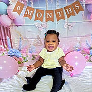 Zoey joined the competition — help win amazing prizes! baby, child, smiling, balloon, banner, 6_months, half_year, celebration, portrait, sitting, yellow_top, black_pants, curly_hair, beads, decorations, floral_backdrop, butterflies, pastel_colors, happy, indoor