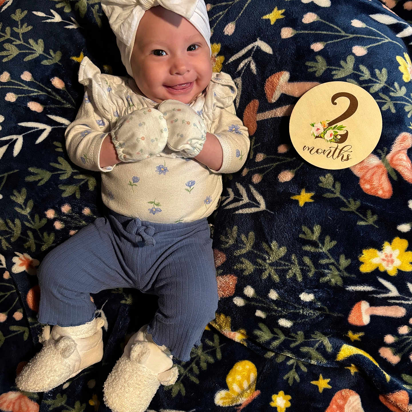Azariah is registered to the contest to win money with this photo: baby, blanket, booties, bow, child, clothing, cute, floral_pattern, happy, headband, indoors, infant, lying_down, milestone_card, mittens, pants, person, portrait, smiling, soft_texture