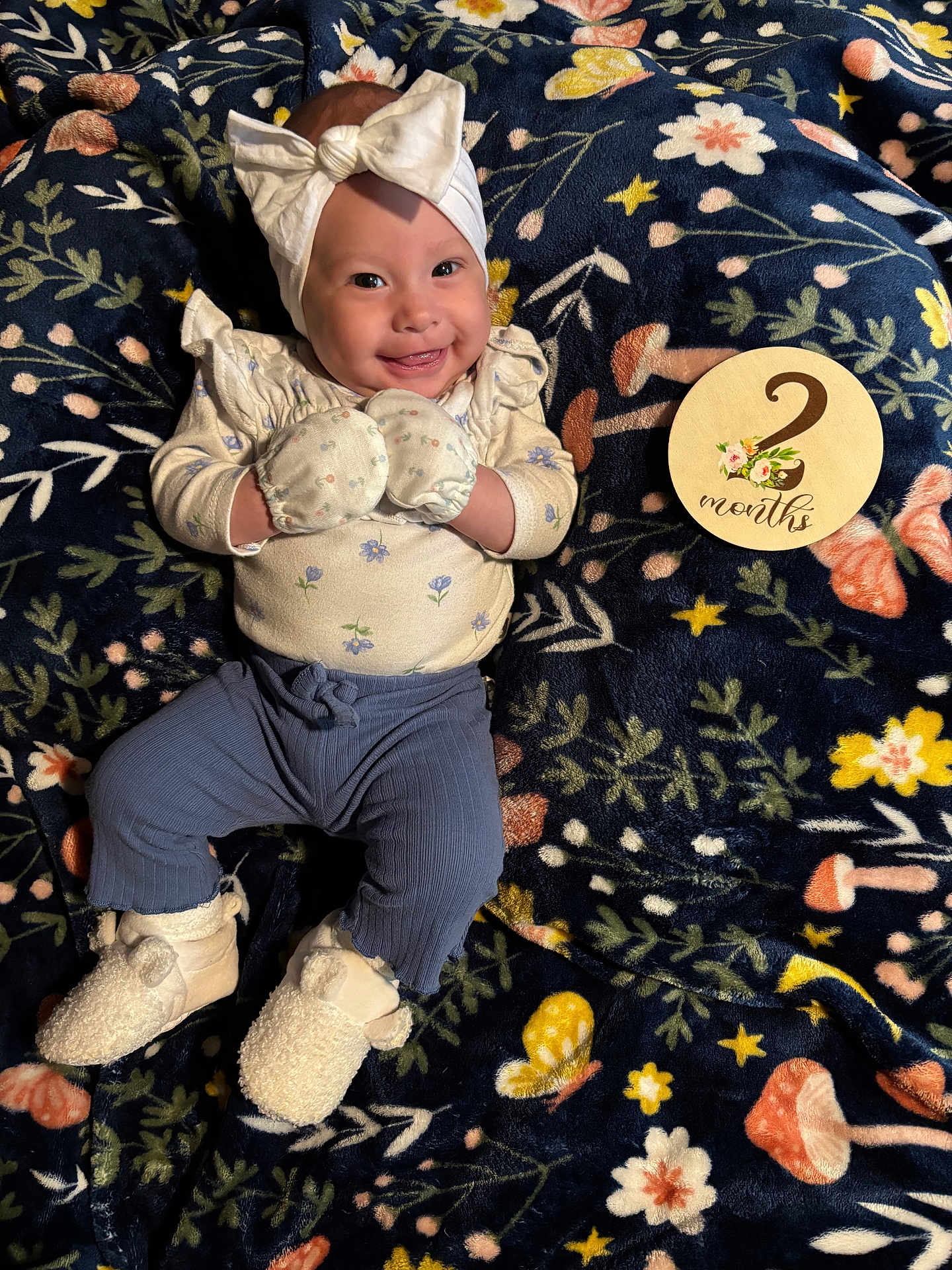 Azariah is registered to the contest to win money with this photo: baby, smiling, mittens, headband, bow, milestone_card, blanket, floral_pattern, pants, booties, infant, cute, lying_down, happy, indoors, soft_texture, child, clothing, person, portrait