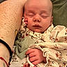 newborn, baby, sleeping, infant, portrait, closeup, face, hand, floral_clothing, onesie, green_toy, soft_blanket, cushion, adult_arm, cozy, indoors, resting, peaceful, family, nap