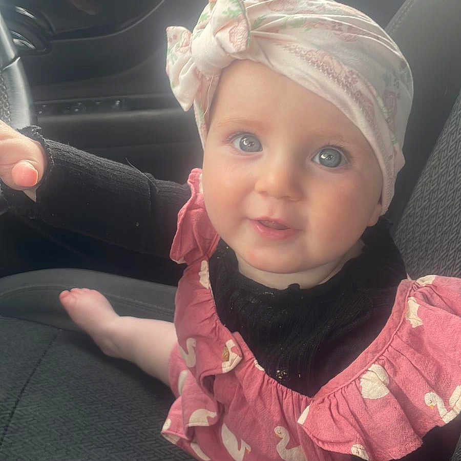 Isla-Jayne is registered to the contest to win money with this photo: baby, blue_eyes, car_interior, car_seat, child, clothing, cute, hand, head_wrap, human, indoors, infant, person, pink_clothing, portrait, seat, sitting, smiling, sock, young_child