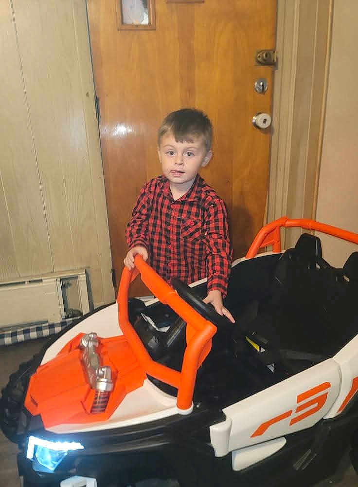 Karson joined the competition — help win amazing prizes! child, boy, toy_car, indoor, red_shirt, checkered_shirt, steering_wheel, wooden_door, paneled_wall, floor, head, face, person, vehicle, play, childhood, young, casual, furniture, room