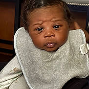 Khyze is registered to the contest to win money with this photo: baby, infant, face, bib, clothing, curious_expression, closeup, child, human, indoor, person, skin, cute, young, newborn, portrait, sitting, black_hair, soft_lighting, comfortable
