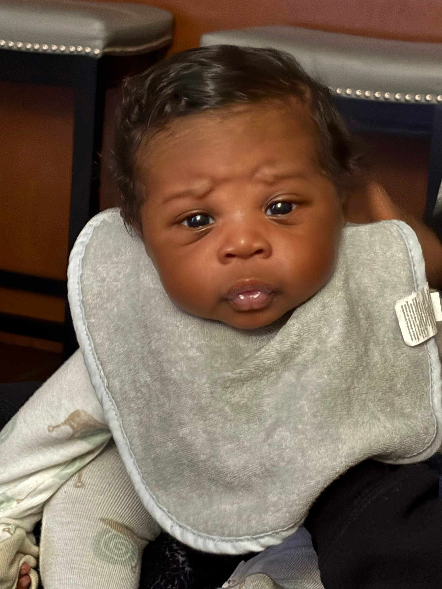 Khyze is registered to the contest to win money with this photo: baby, infant, face, bib, clothing, curious_expression, closeup, child, human, indoor, person, skin, cute, young, newborn, portrait, sitting, black_hair, soft_lighting, comfortable